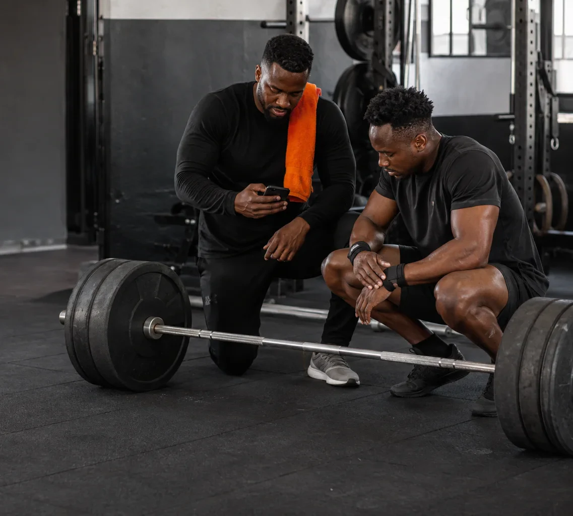 Coach and athlete reviewing a session together beside a loaded barbell